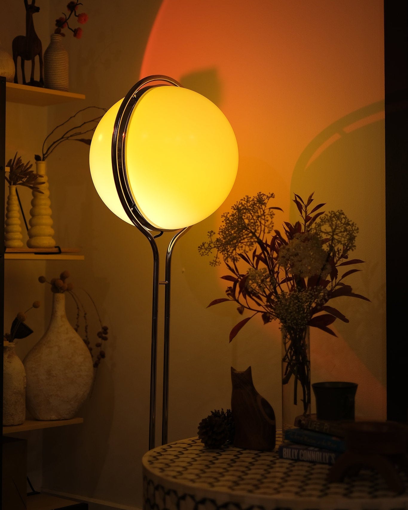 Floor lamp with a warm glow in a dimly lit room with decorative items. Garreau Globe Floor Lamp Bauhaus Replica Chrome Stand
