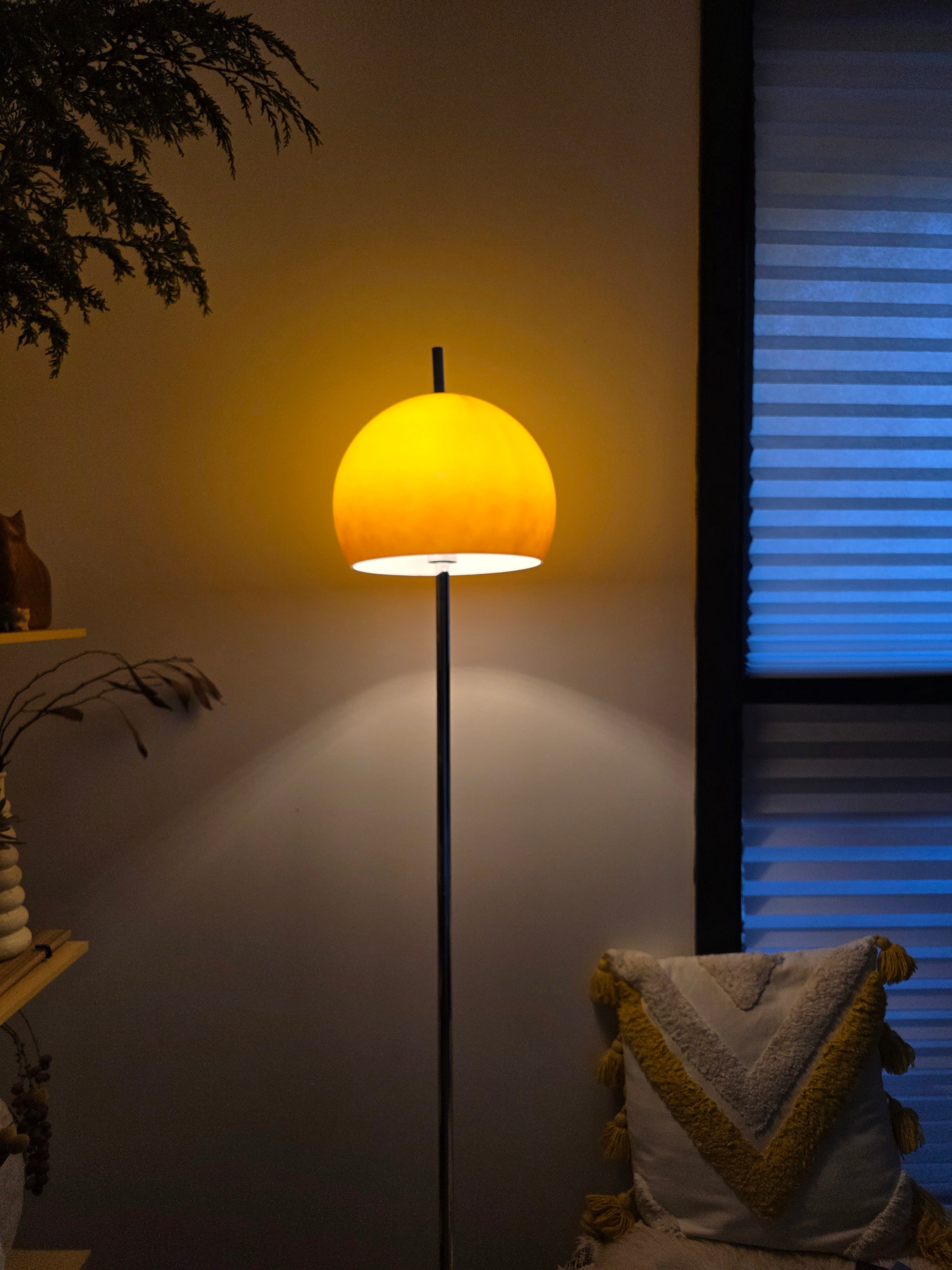 Olivia Mushroom Bauhaus Floor lamp with a round shade emitting a warm glow in a dimly lit room.