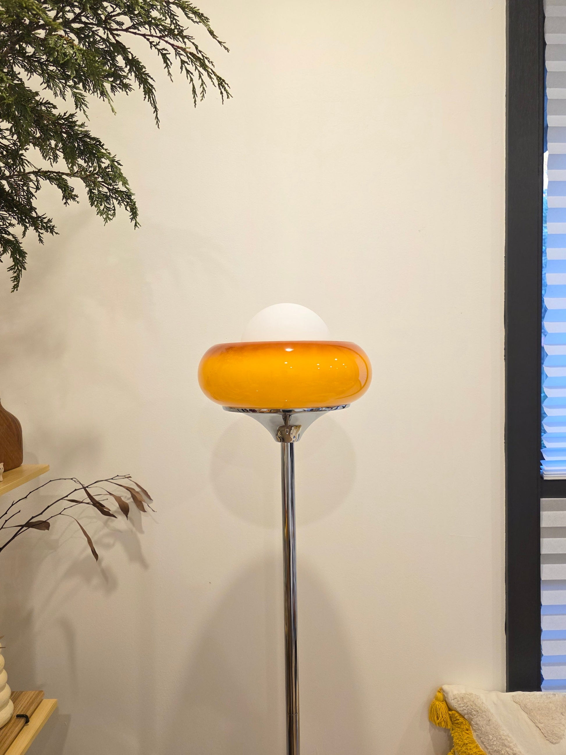 Retro modern Egg Tart Floor Lamp with chrome base with a yellow glass shade against a white wall.