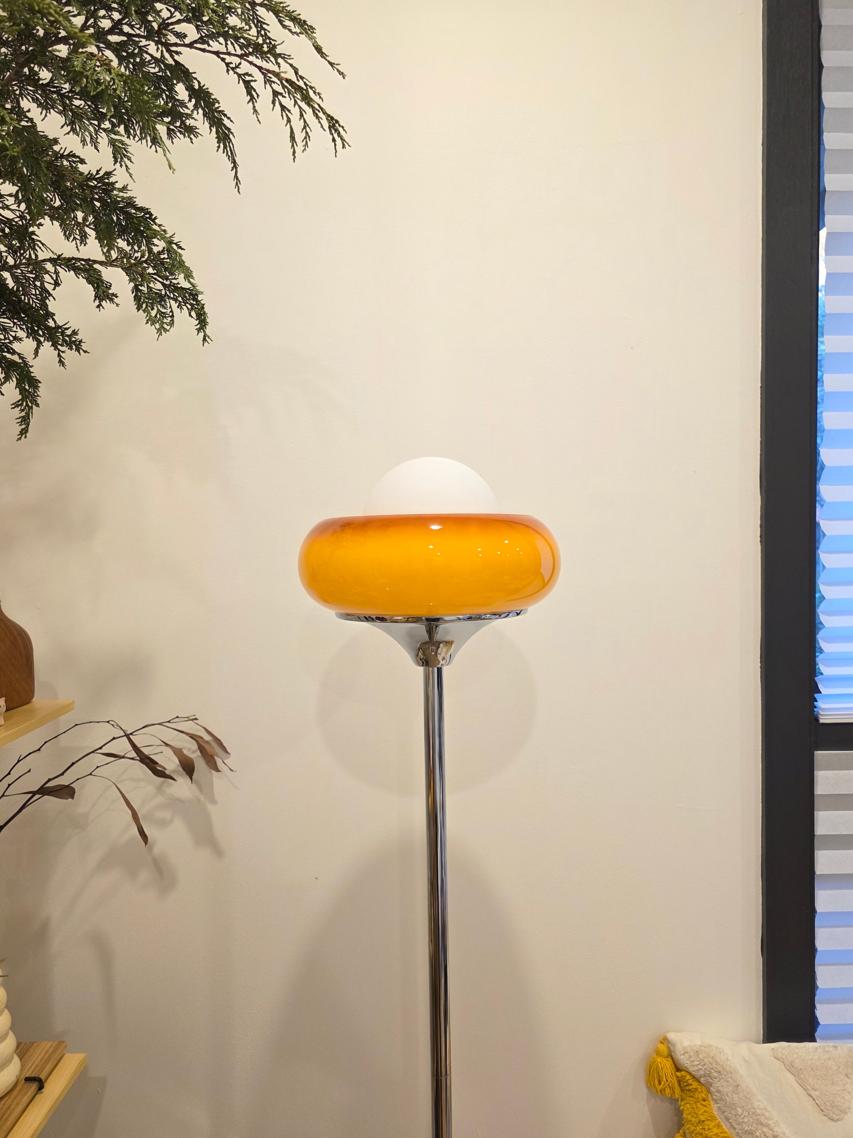 Retro modern Egg Tart Floor Lamp with chrome base with a yellow glass shade against a white wall.