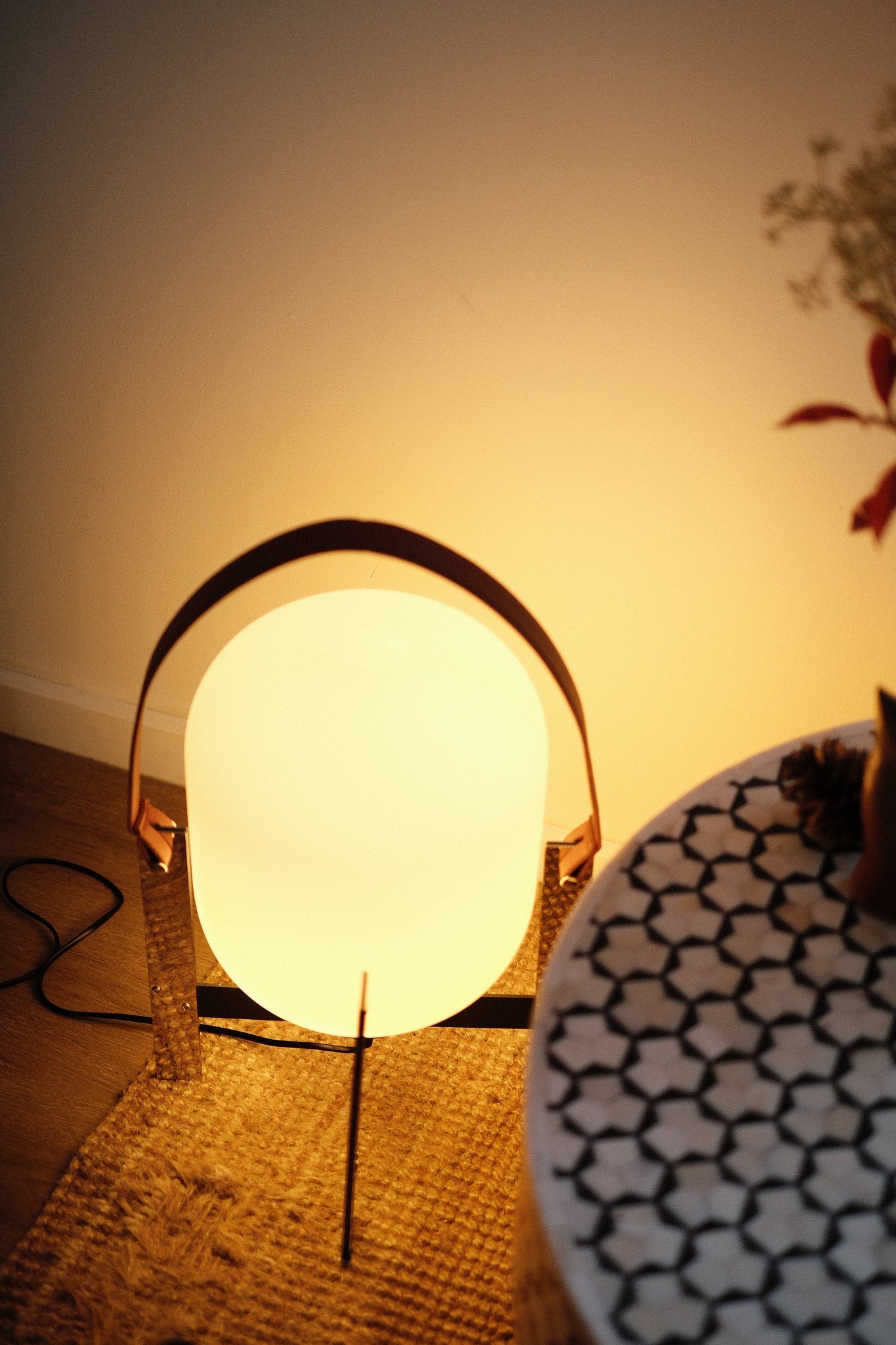 Alix Cesta Metalica Basket Lamp with chrome frame and opal glass globe with a warm glow on a textured surface
