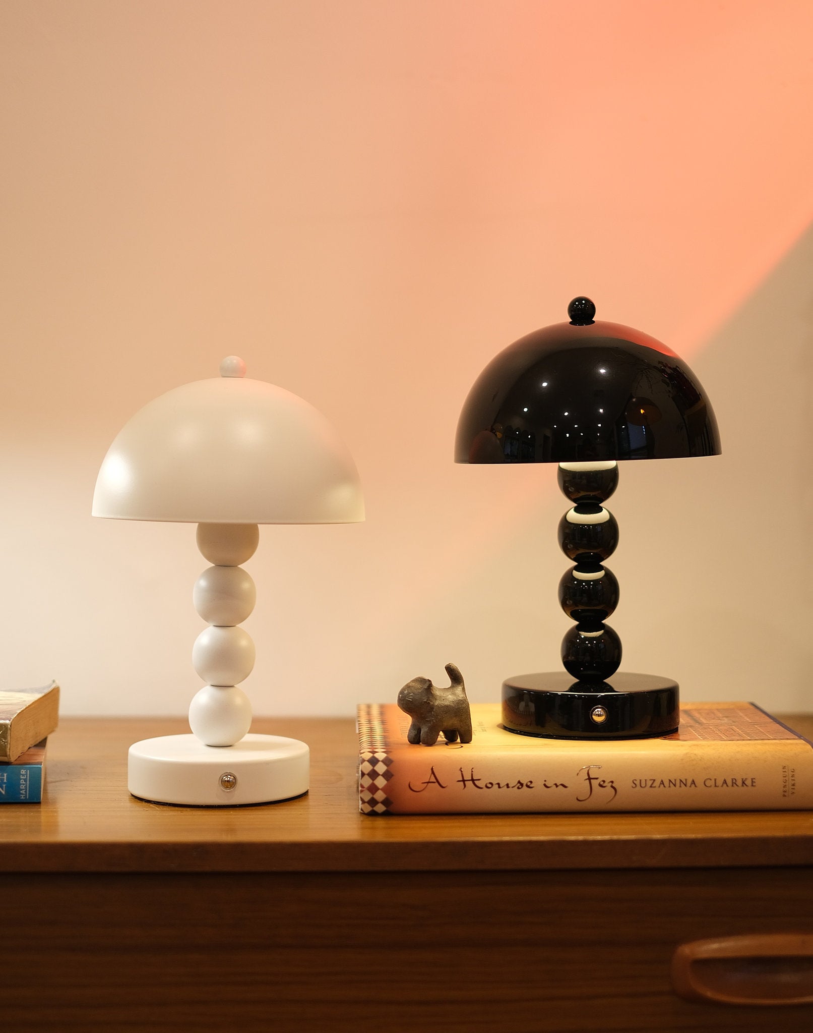 Two Bobbi Portable LED Table Lamp in white lacquer finish on bedside table on a wooden surface with a book and small figurine in the background.