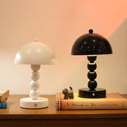 Two Bobbi Portable LED Table Lamp in white lacquer finish on bedside table on a wooden surface with a book and small figurine in the background.