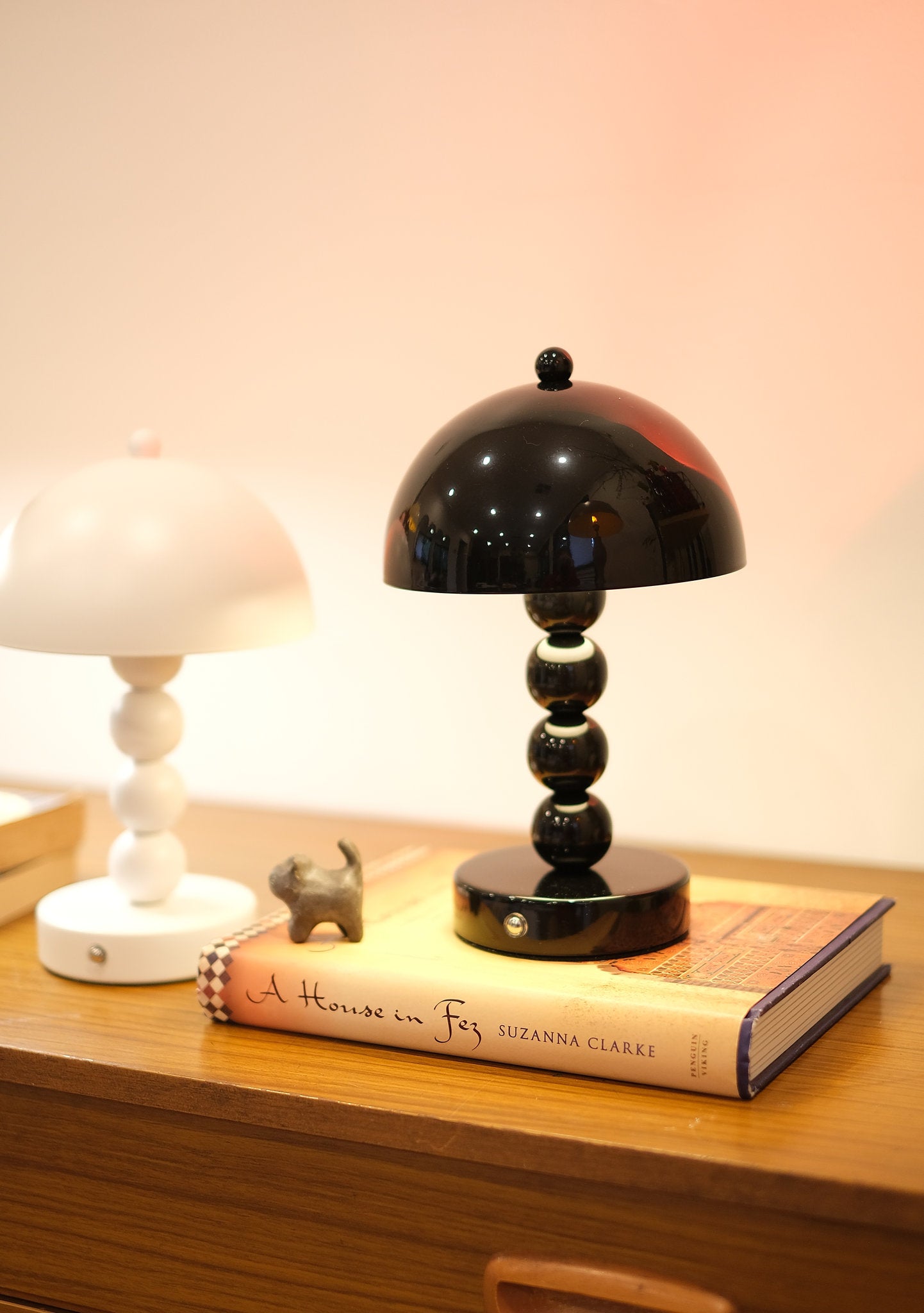 Bobbi Portable LED Table Lamp in white lacquer finish on bedside tableon a wooden surface with a book and small figurine