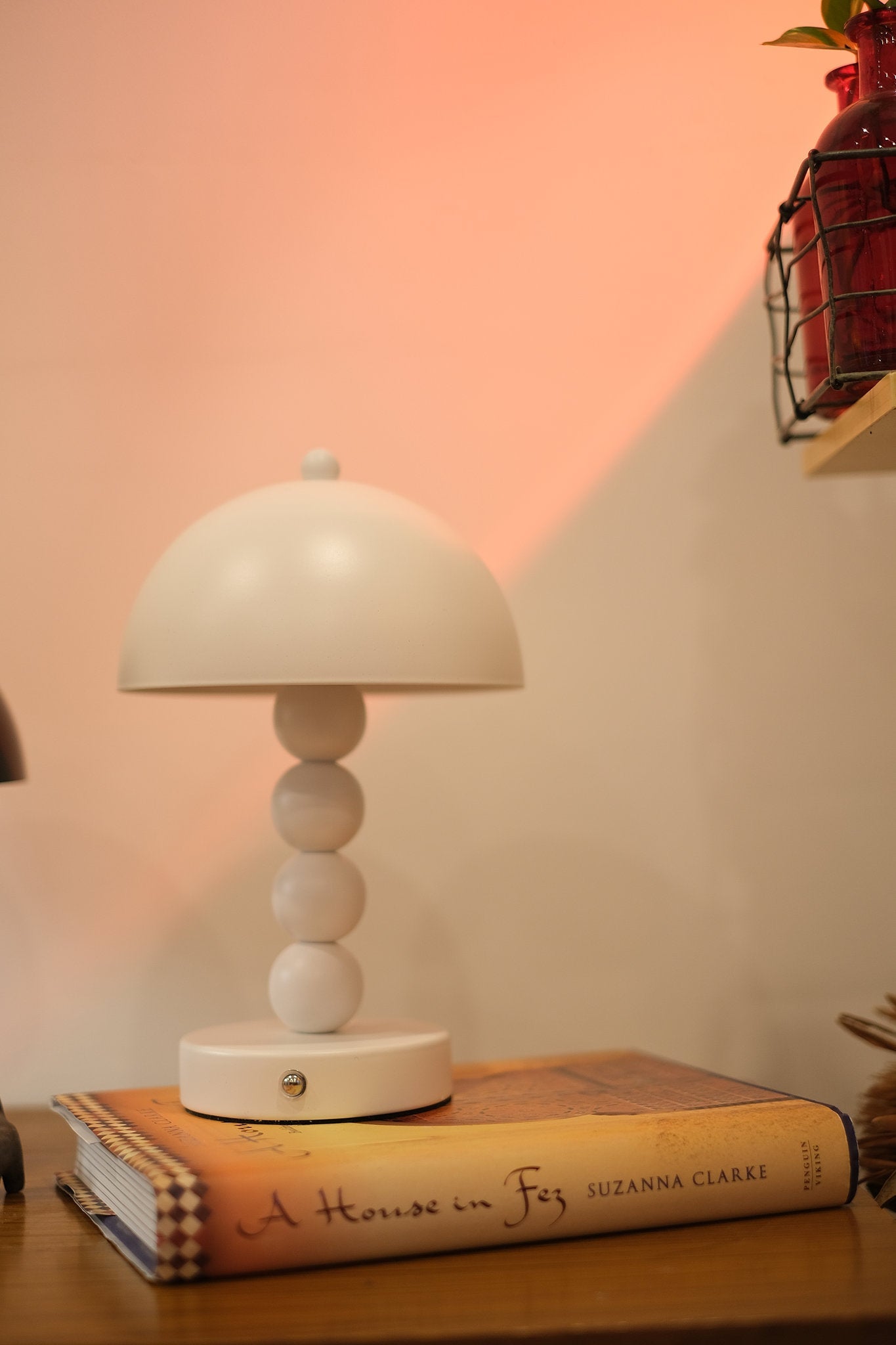 Touch dimmable Bobbi lamp in Nordic minimalist décor on a stack of books with a warm pinkish-orange glow in the background