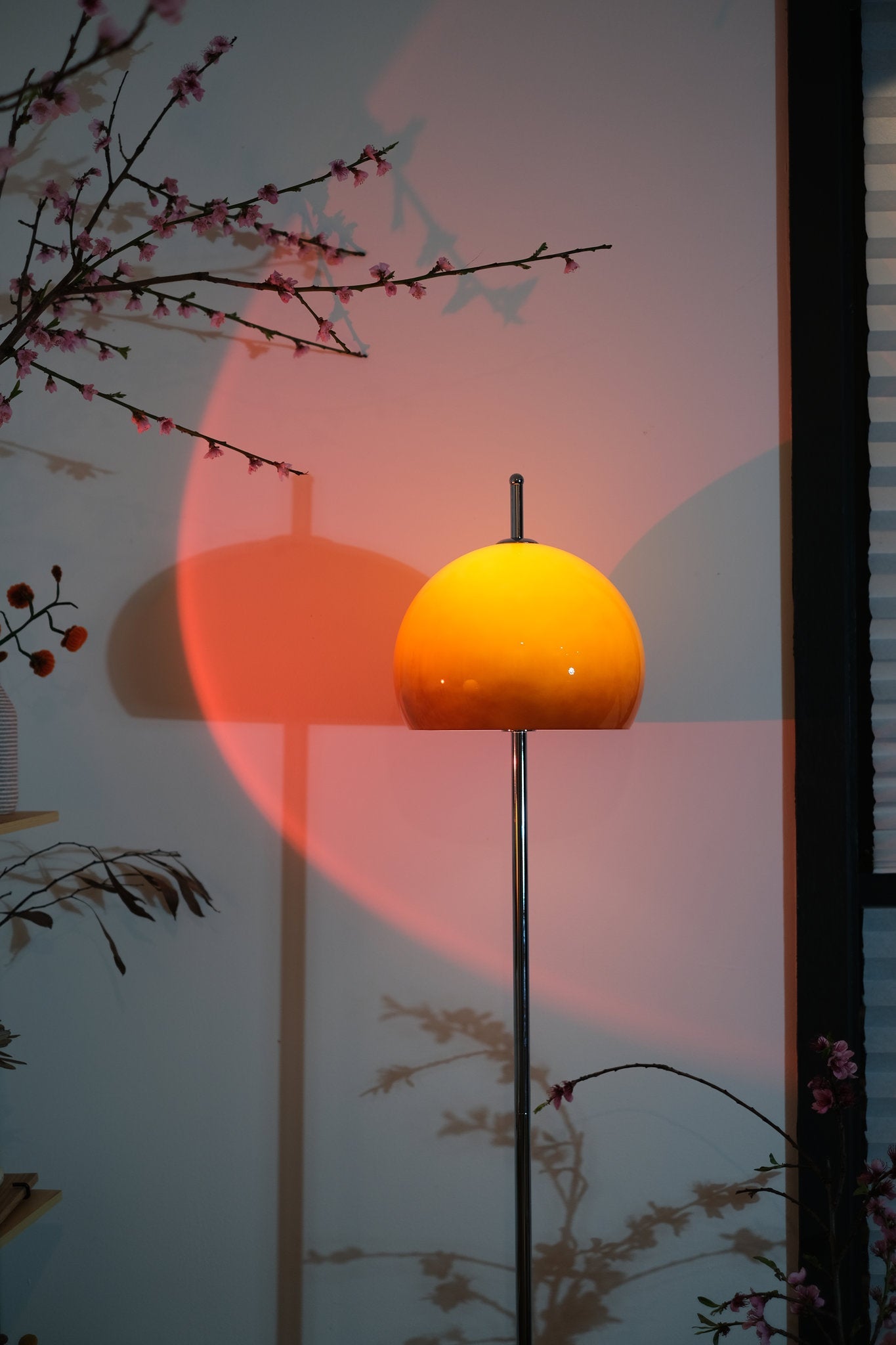 Olivia Mushroom Bauhaus spherical lamp on a pole with a pink and orange gradient light and floral branches.