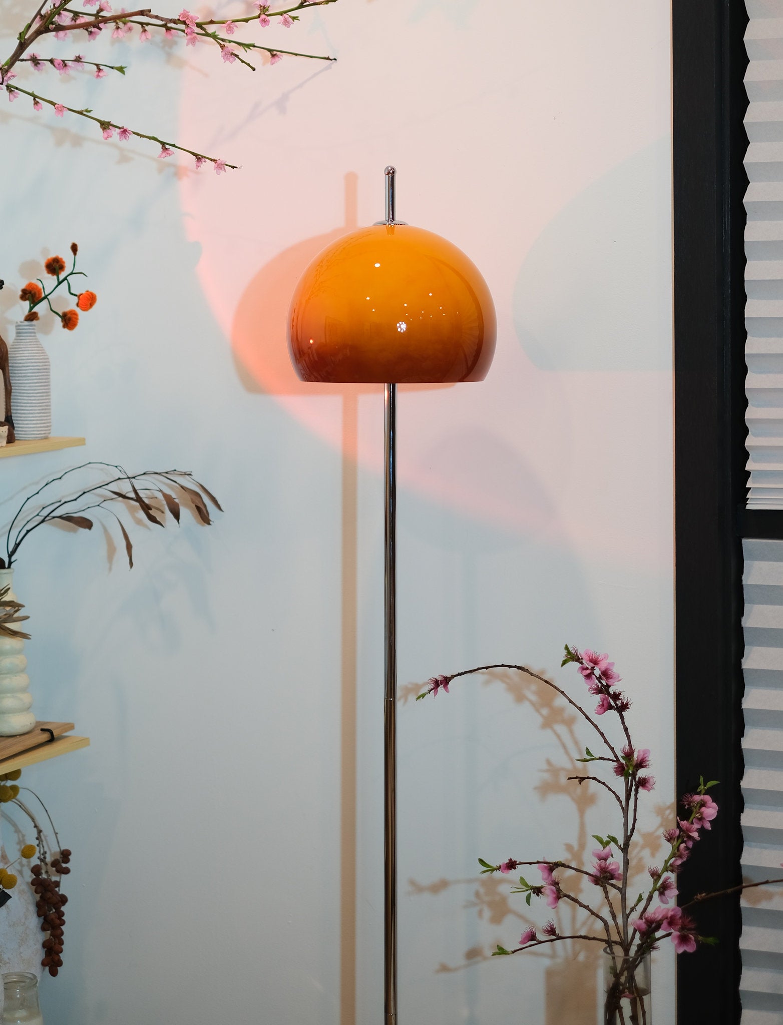 Olivia Mushroom Bauhaus Floor lamp with an orange shade in a room with decorative plants and a vase.