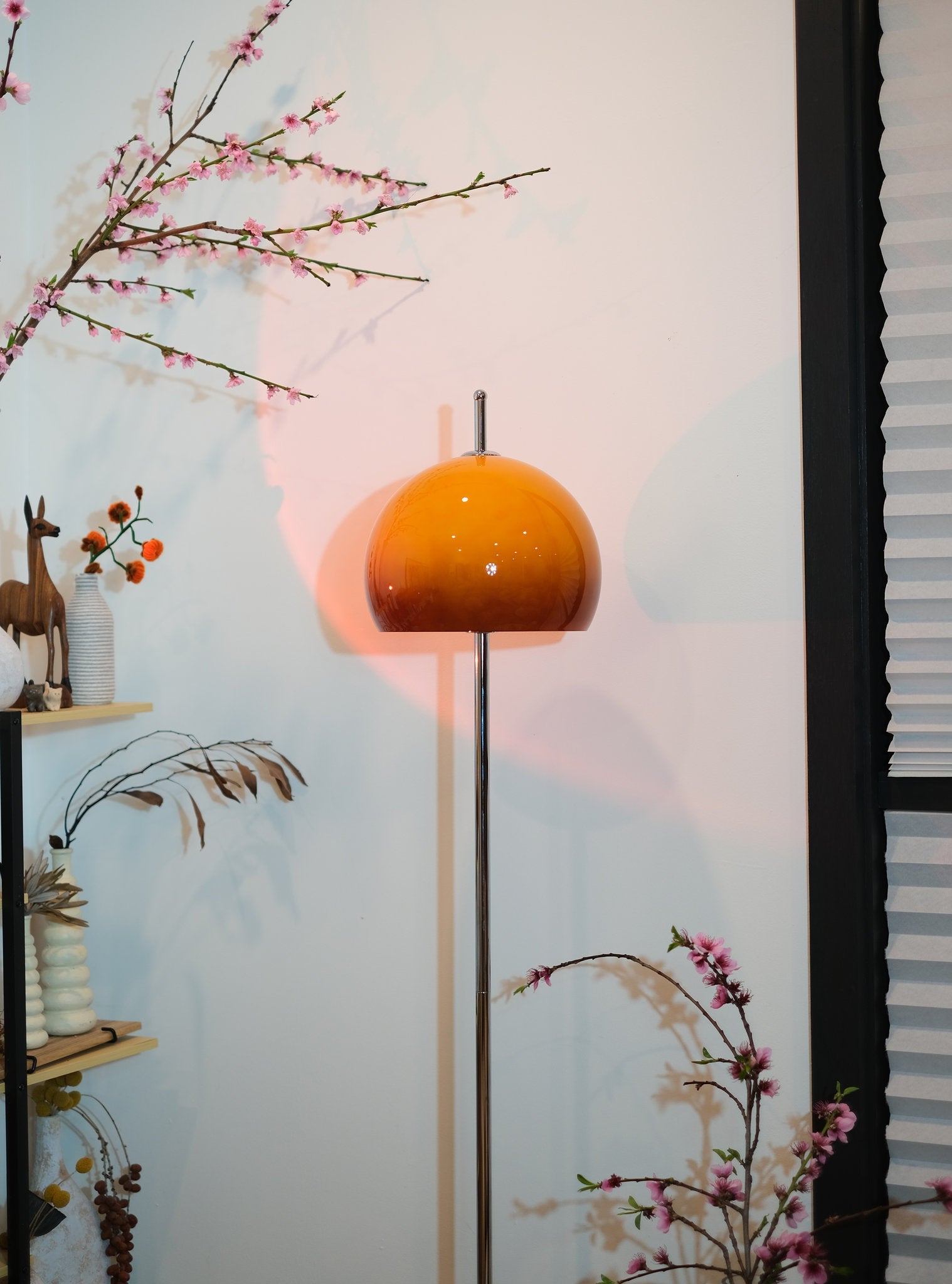 Olivia Mushroom Bauhaus floor lamp with an orange shade in a room with floral branches and shelves.