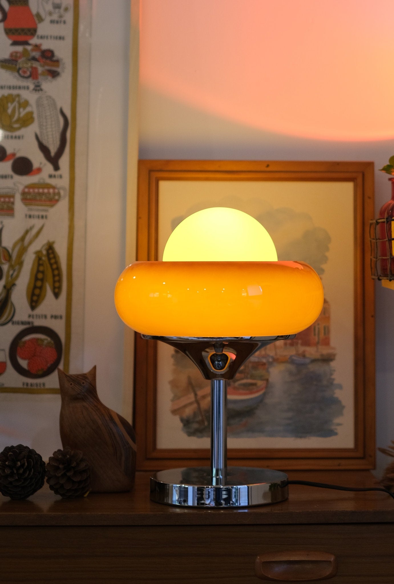 Egg Tart Table Lamp with orange dome glass shade and white inner globe on a table with a cat and framed picture in the background