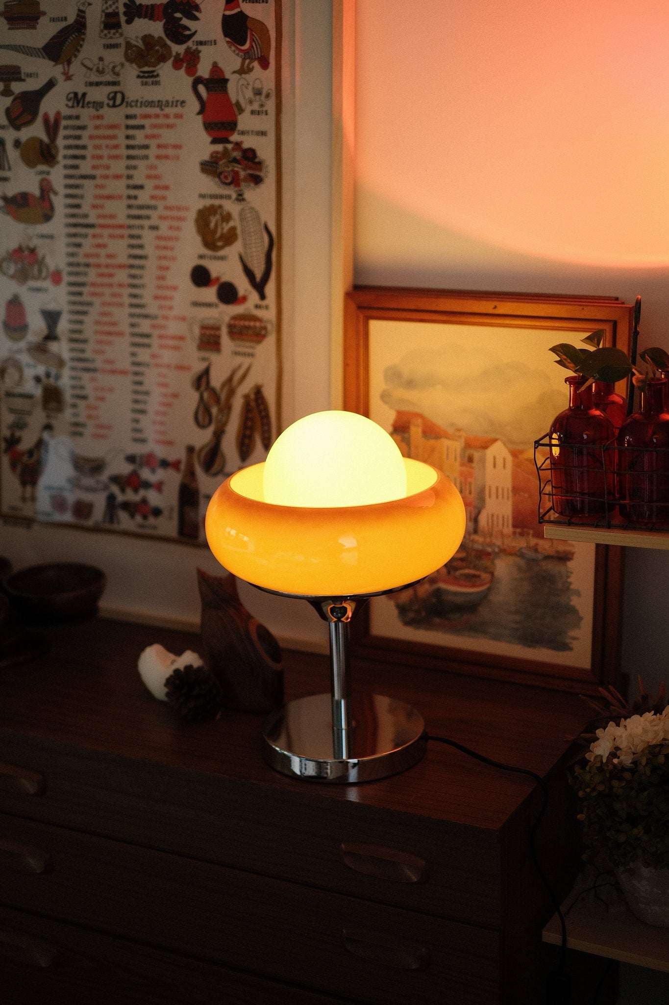 Egg Tart Table Lamp with orange dome glass shade and white inner globe on a wooden surface with a warm glow, surrounded by decorative items.