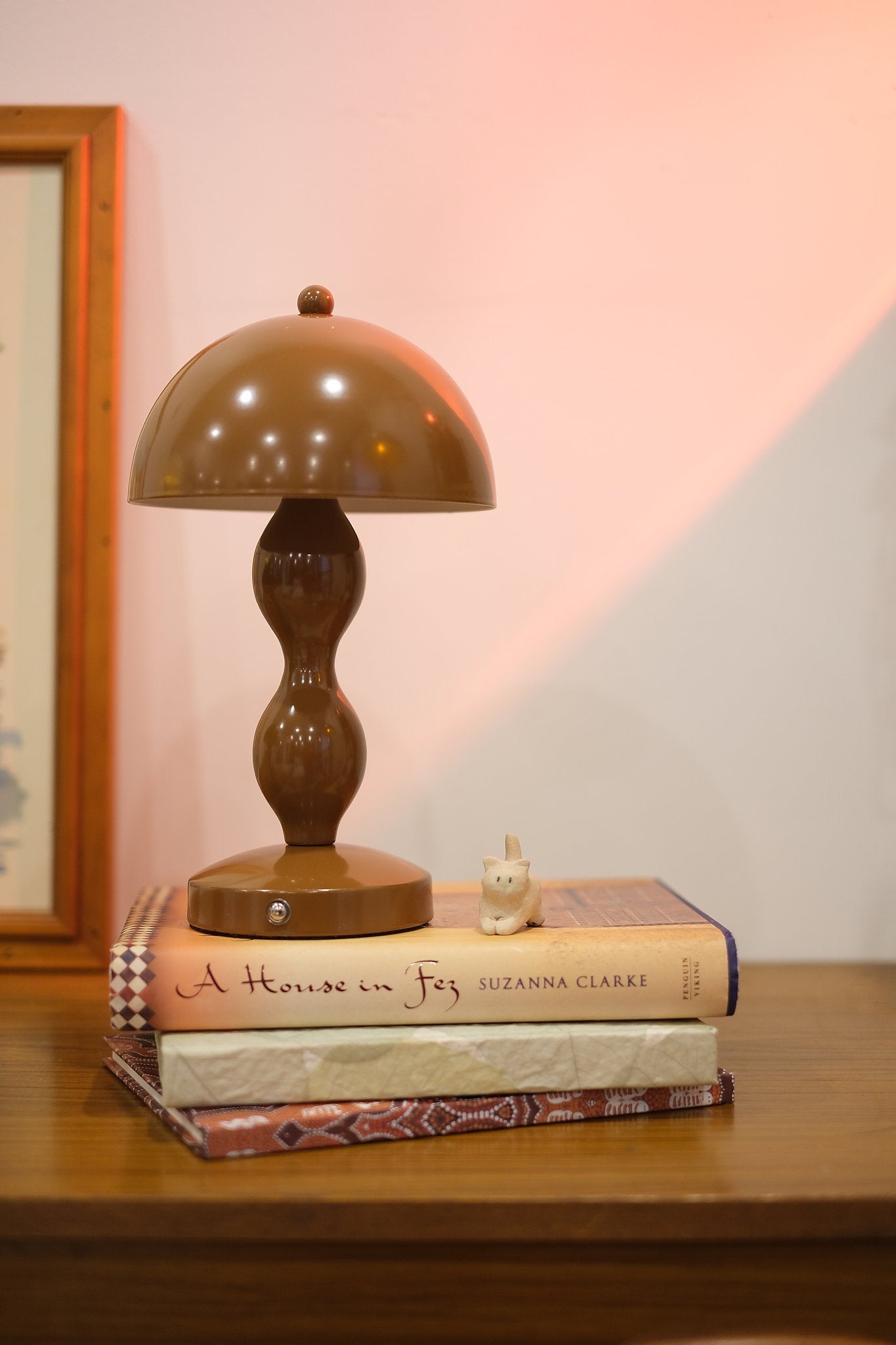 Retro mushroom lamp glowing softly in modern interior décor on a stack of books with a soft pink wall in the background