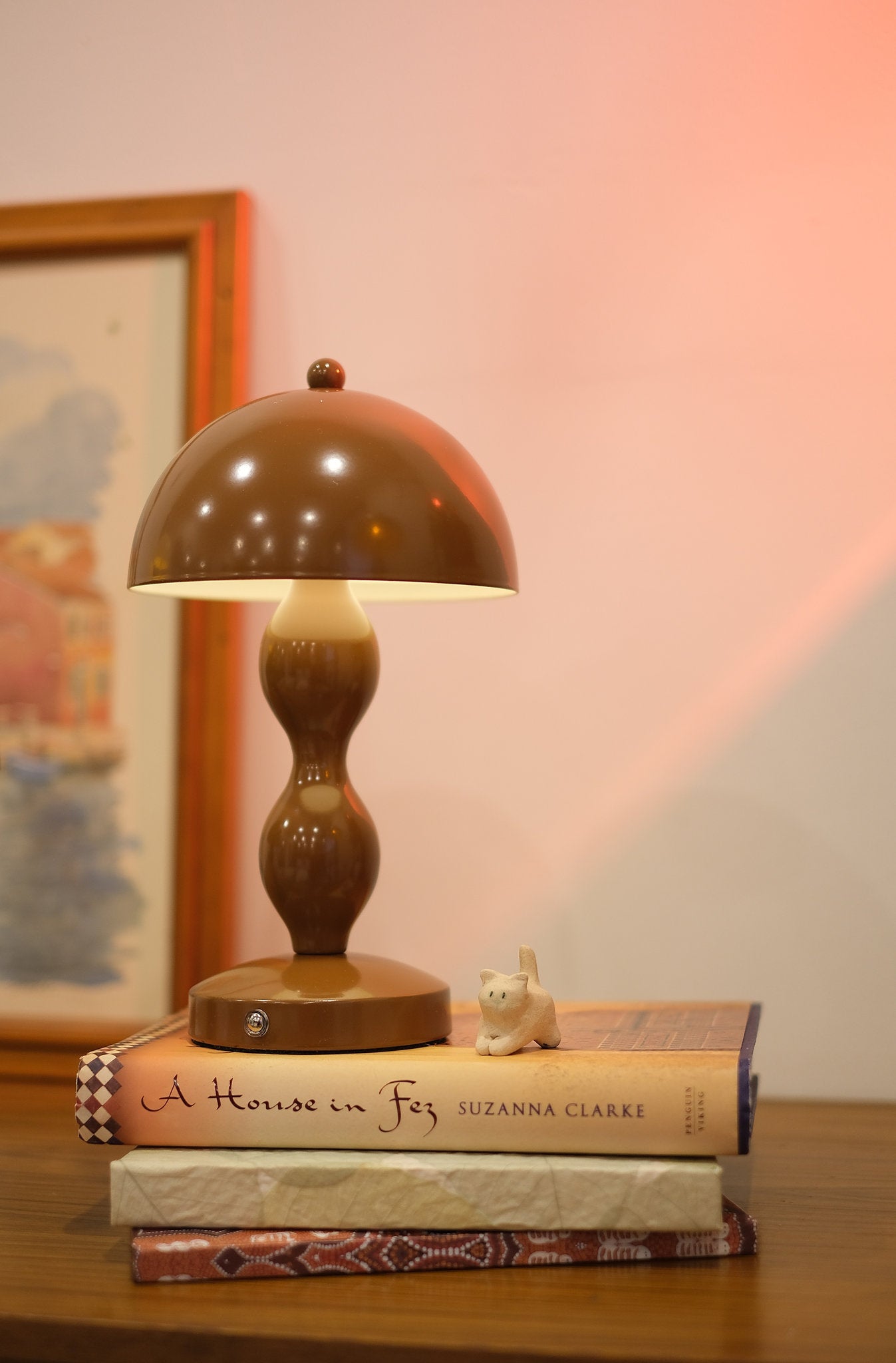 Dori LED lamp close-up showing touch switch base on a stack of books with a blurred painting in the background