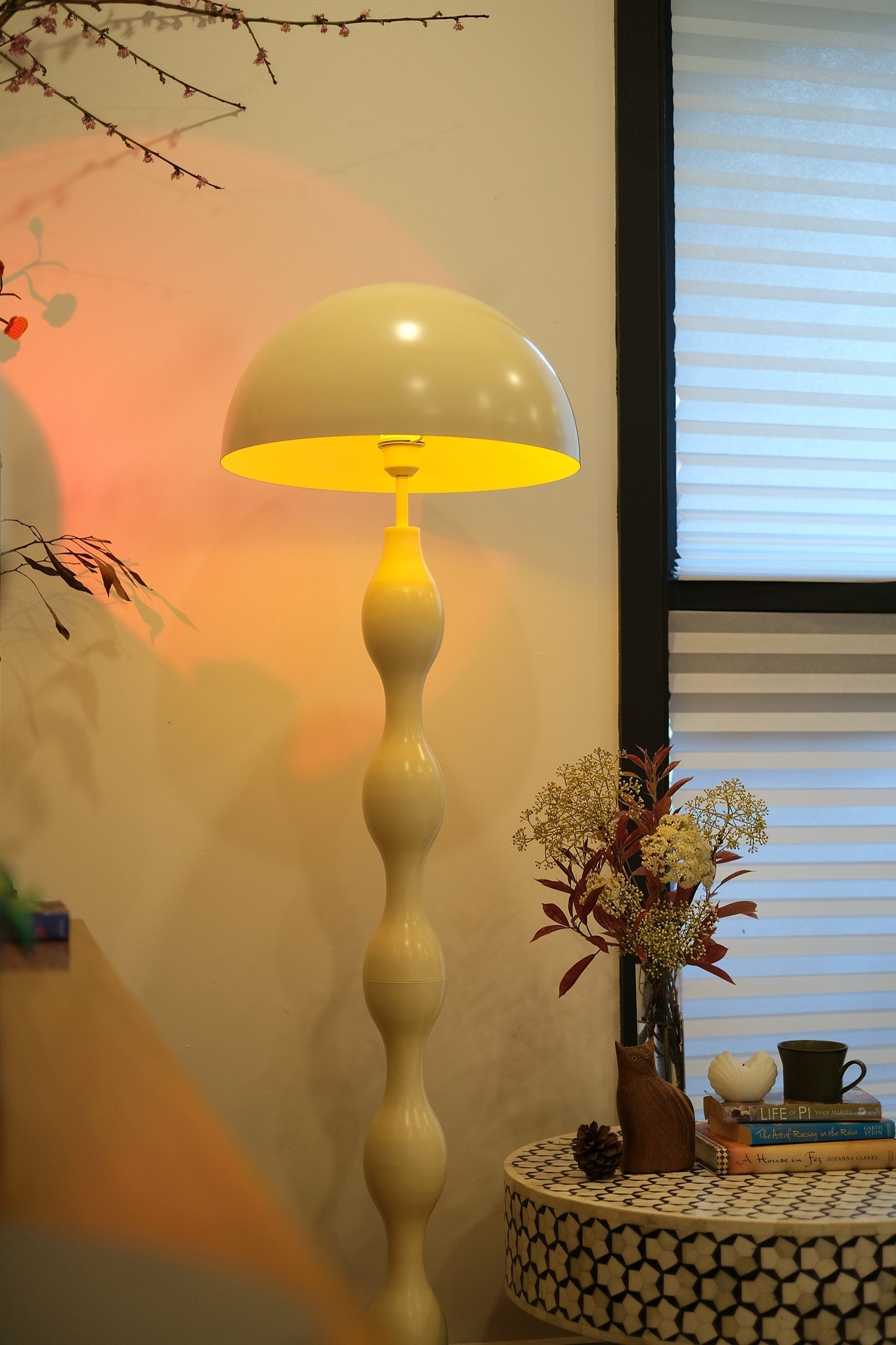 Dori Wavy Mushroom Floor Lamp in Butter Yellow casting warm ambient glow  in a room with a table and decorative items.