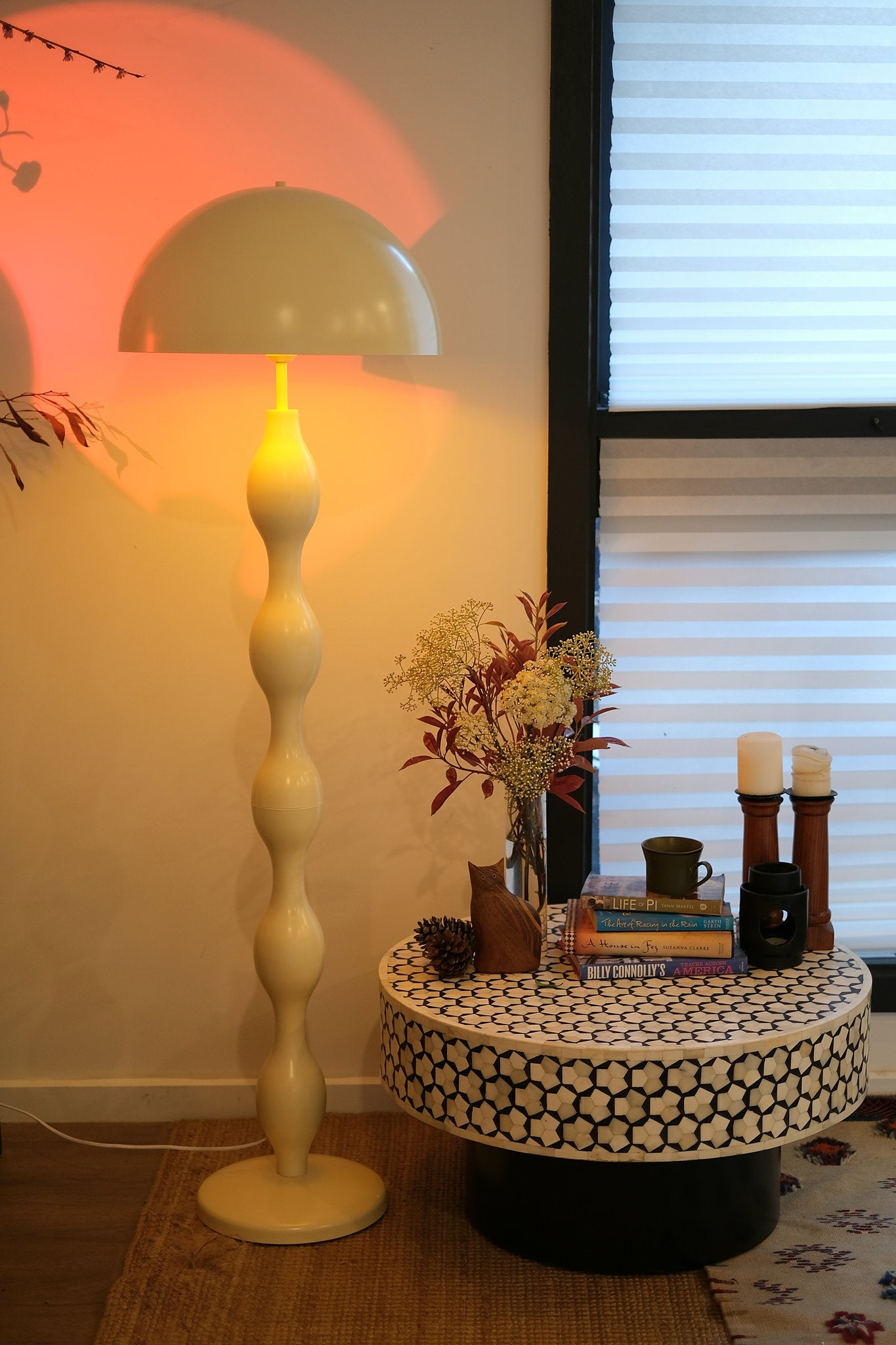 Funky butter yellow mushroom lamp styled in a modern living room next to a small round table with candles and books in a room.