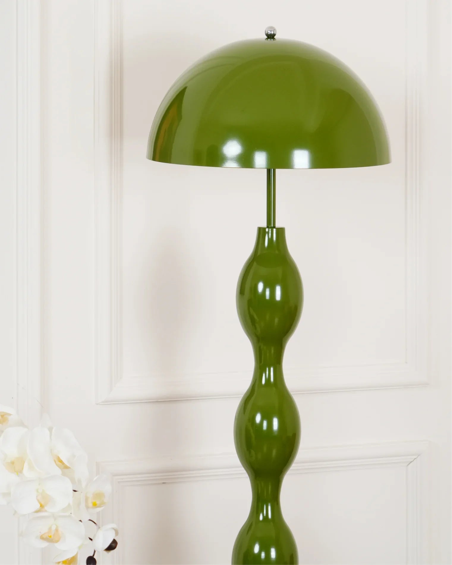 Dori Wavy Mushroom Floor Lamp in Olive Green with sculptural wavy base against a white wall with a decorative plant in the foreground.