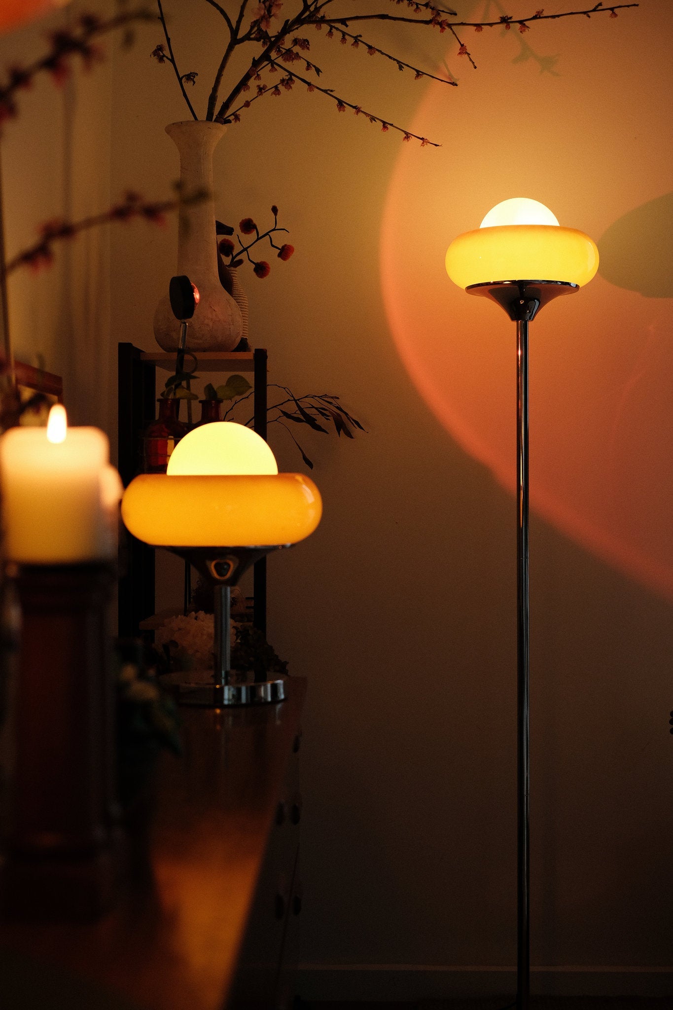 very Egg Tart retro lamp duo – sculptural glass dome floor lamp and table lamp for cozy spaces casting warm light on a wall with a candle and decorative items in the foreground.
