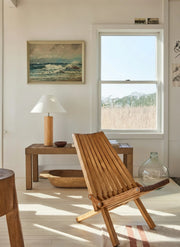 Morgan Table Lamp in Natural Wood with linen shade on bench, Wooden chair in a room with a window and wall art