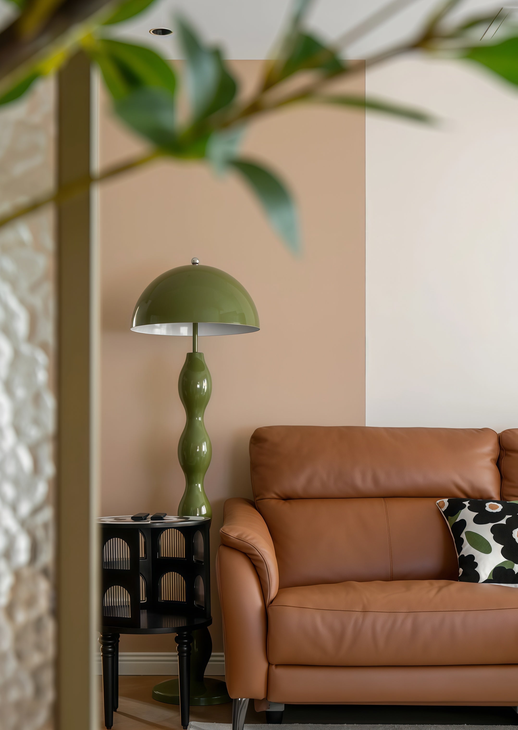 Dori Wavy Mushroom Floor Lamp in Olive Green with sculptural wavy base next to a side table next to a brown leather sofa with a decorative pillow.