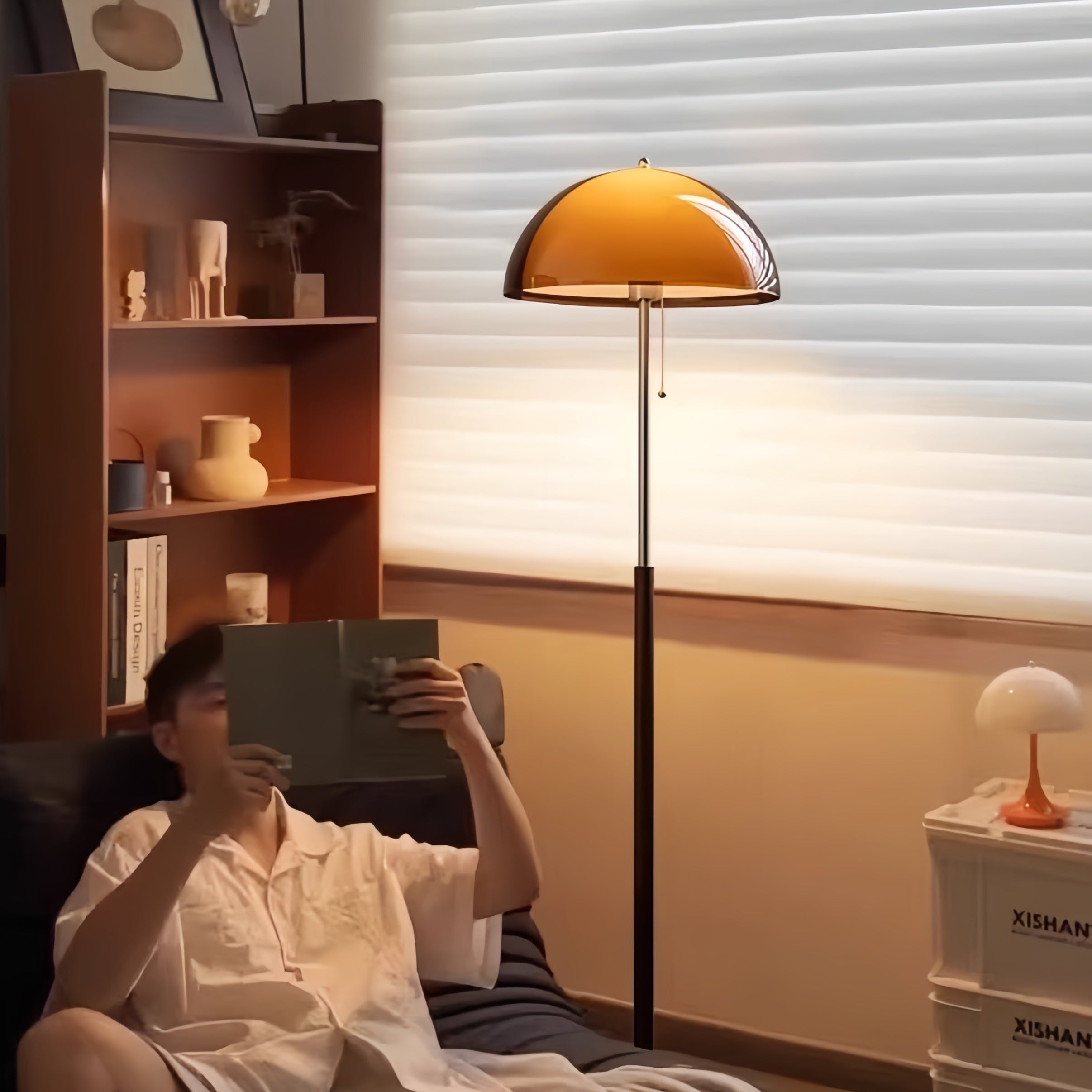 Person sitting on a couch reading a book in a cozy room with a bookshelf and Coby+ Mushroom Bauhaus Floor Lamp Orange with Pull Chain