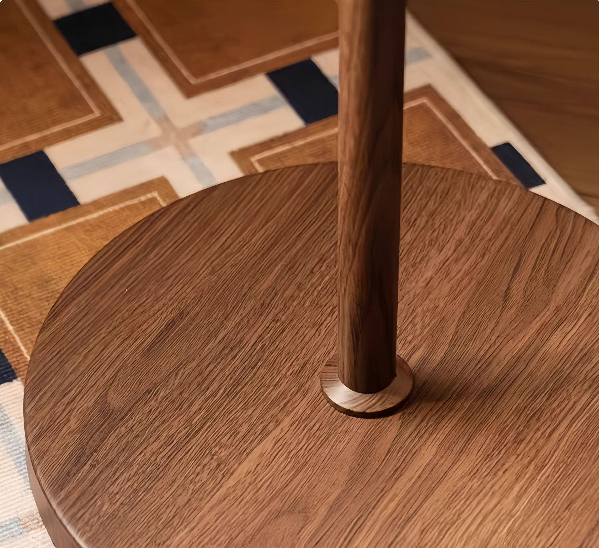 Close-up of a wooden table base with a geometric patterned rug in the background