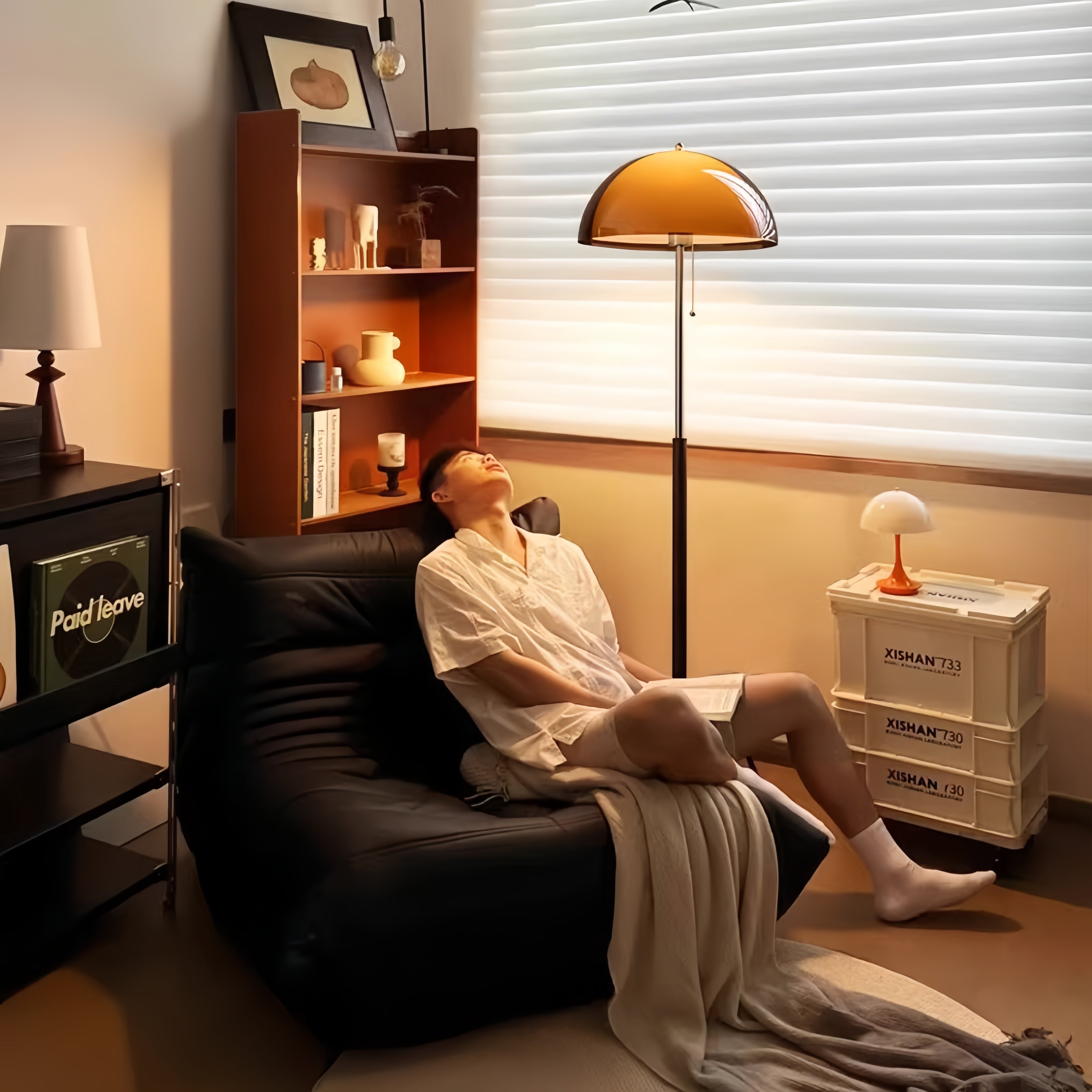 Person sitting on a couch in a dimly lit room with a  shelves and Coby+ Mushroom Bauhaus Floor Lamp Orange with Pull Chain.